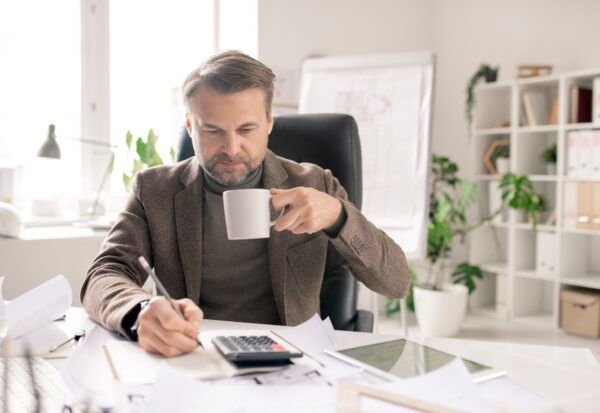 Serious mature accountant with pen and cup of coffee making calculations Serious mature accountant with pen and cup of coffee making calculations